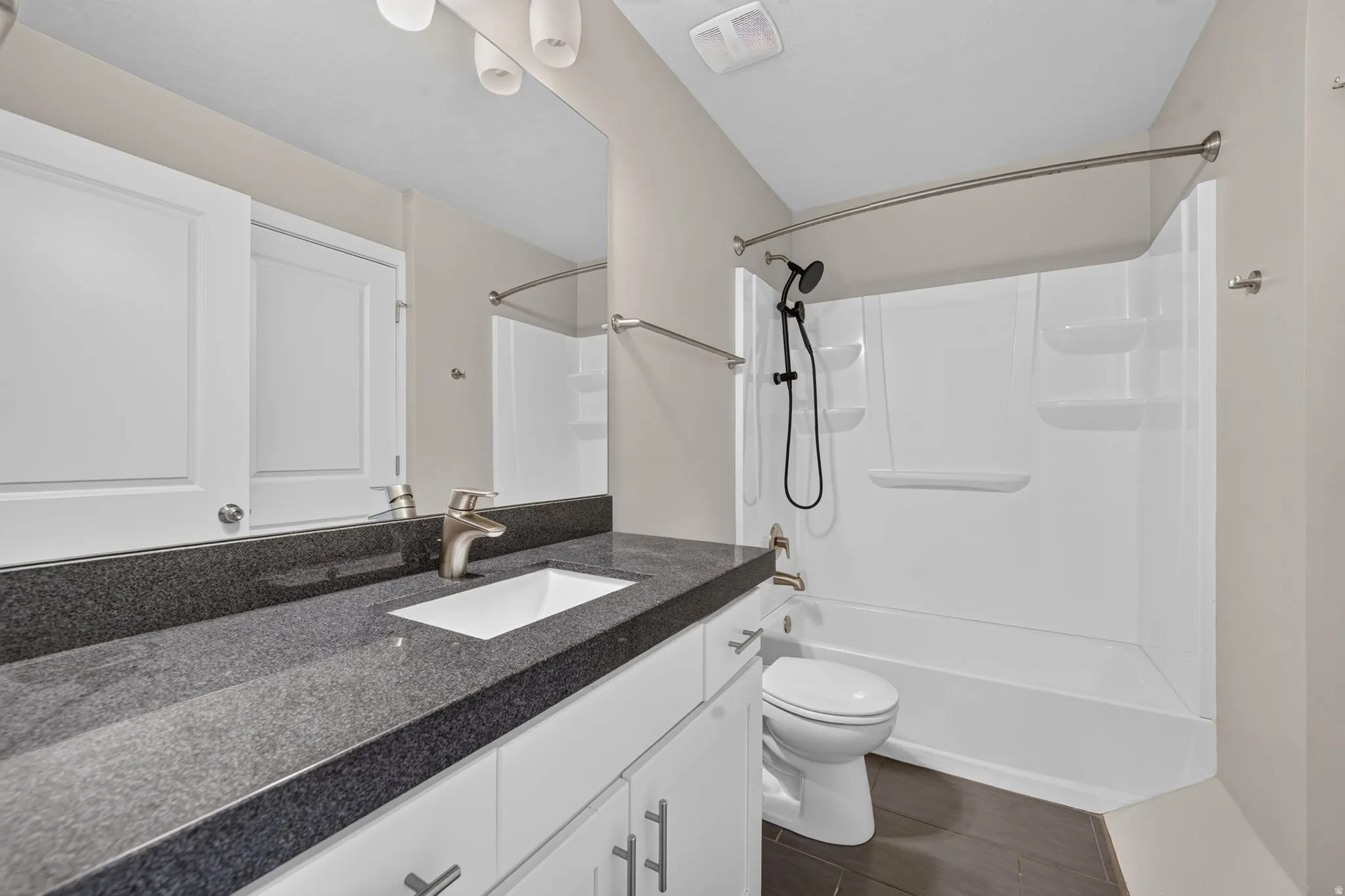 Bathroom featuring a white vanity with brushed nickel hardware, a dark countertop, an undermount sink, and a shower-tub combination with white surround