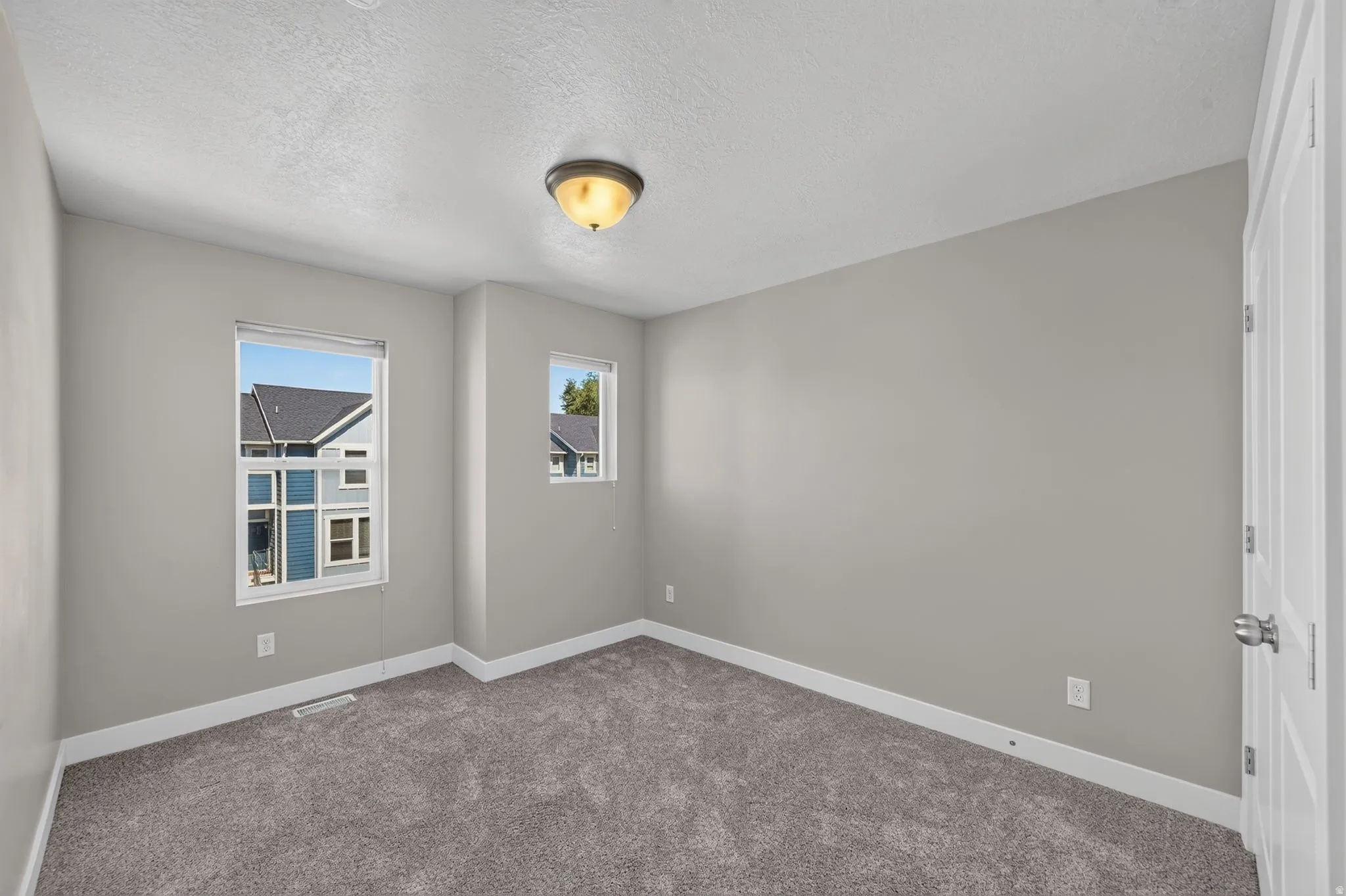 Carpeted interior space featuring light grey walls, white trim, two windows, and a flush-mount ceiling light