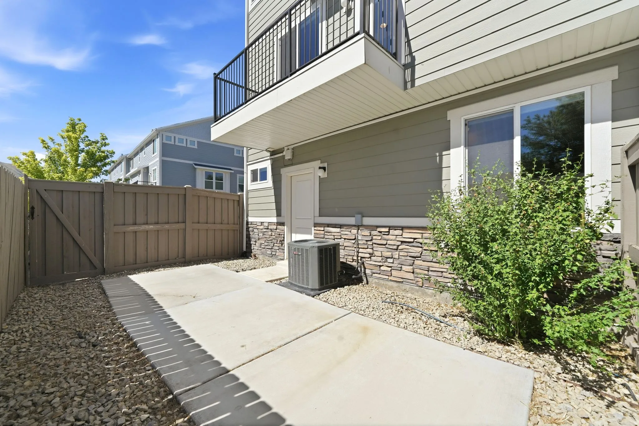 Private outdoor patio featuring a concrete walkway, gravel landscaping, and a wooden privacy fence with gate