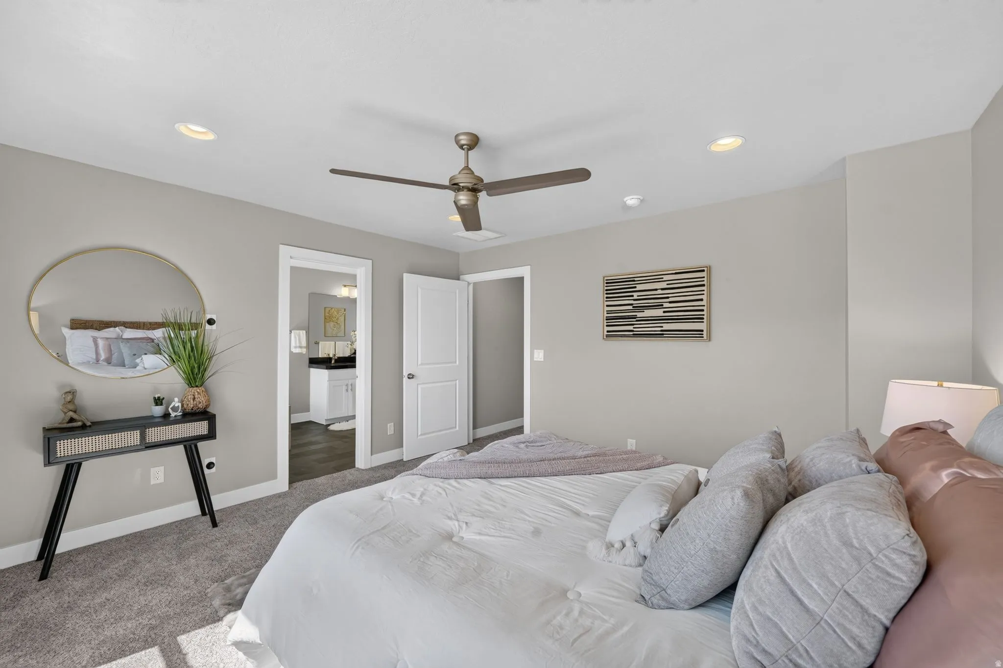 Carpeted room with light gray walls featuring a ceiling fan, recessed lighting, and a doorway opening to a bathroom with a vanity and dark wood-finish flooring