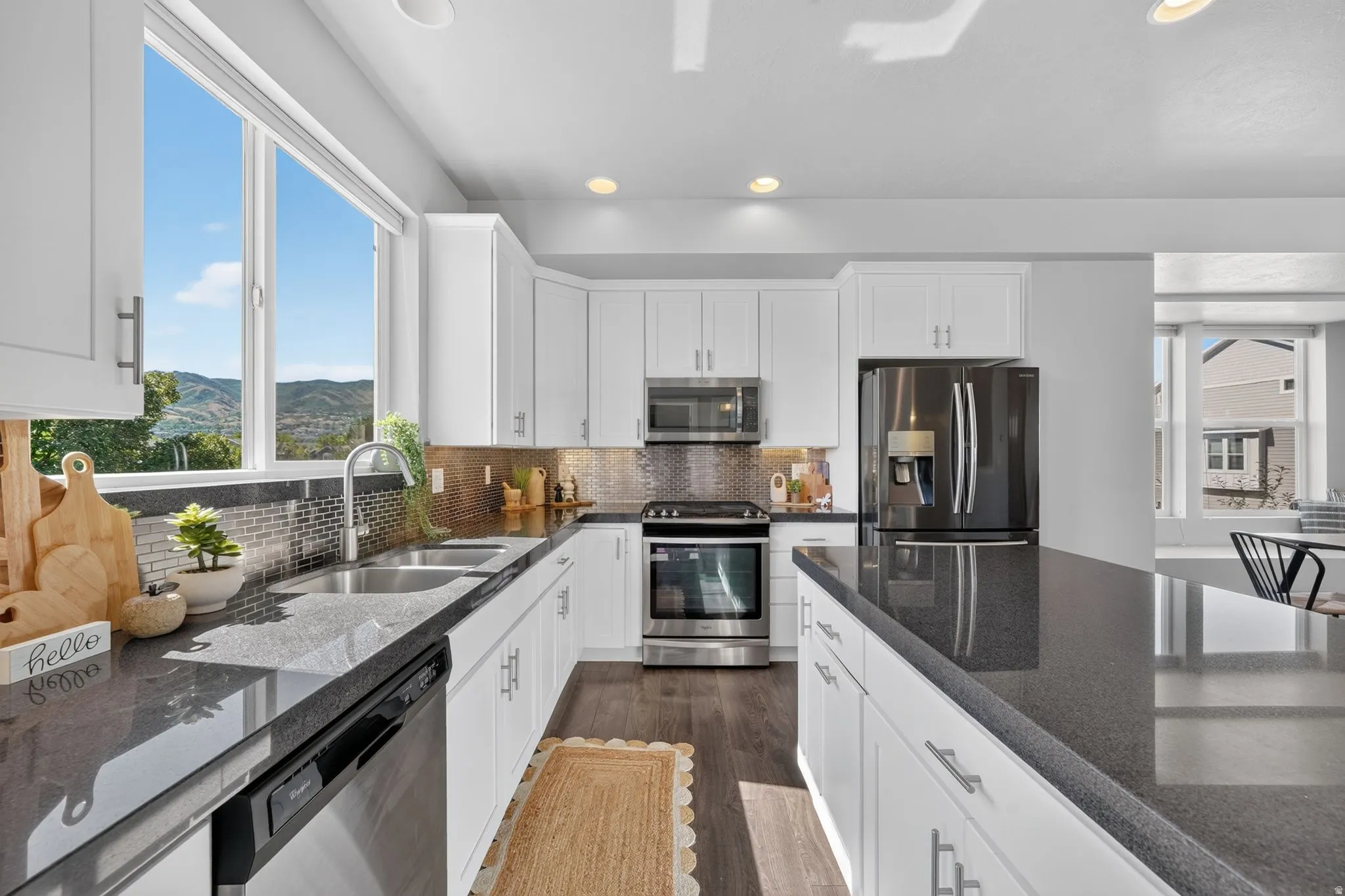 Bright kitchen featuring white cabinetry, dark countertops, stainless steel appliances, a tile backsplash, and wood-finish flooring