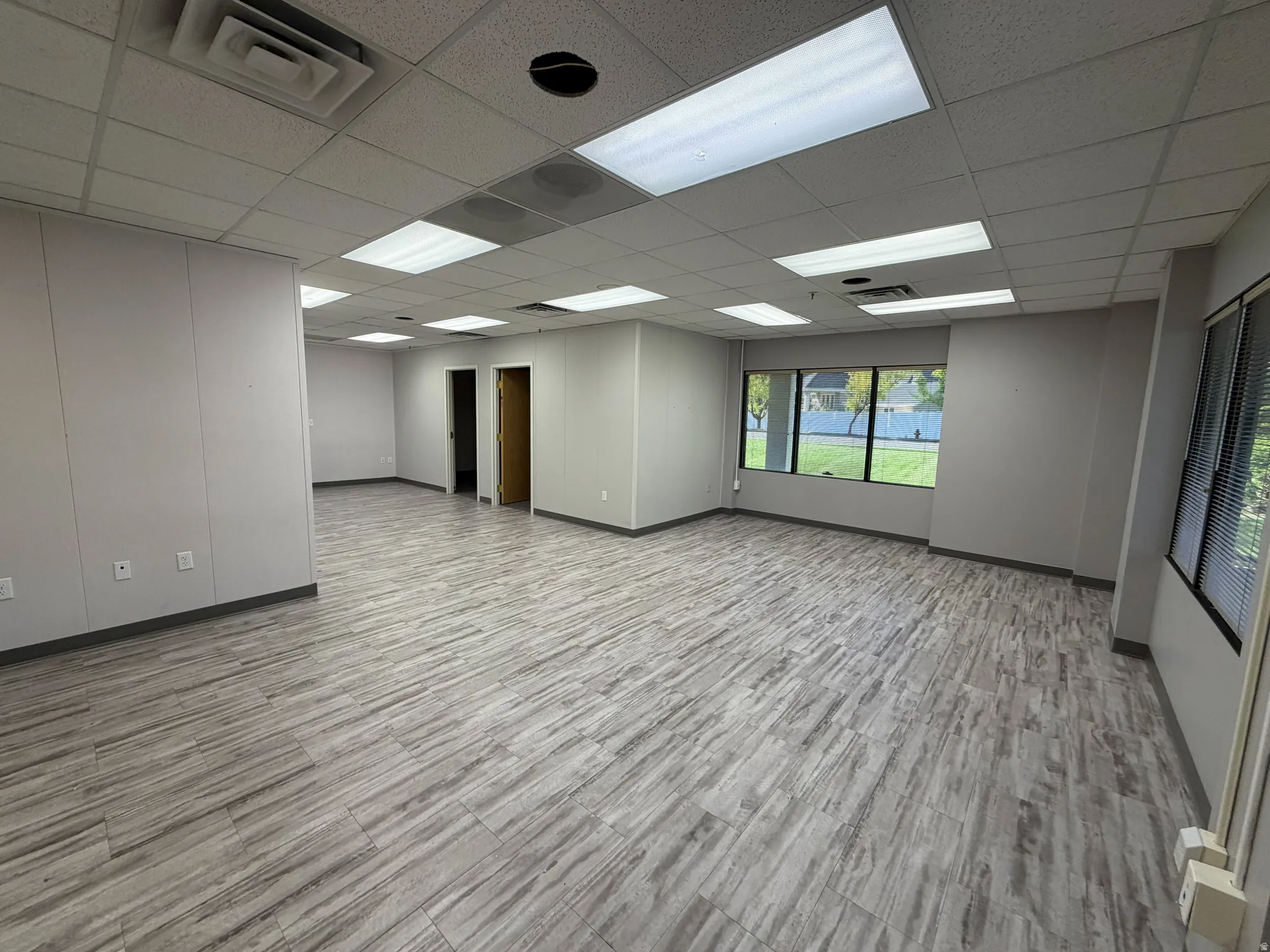 Spacious commercial interior featuring plank-style flooring, a drop ceiling with recessed lighting, and multiple large windows for natural illumination