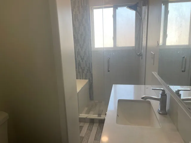 White vanity with an integrated rectangular sink, brushed nickel faucet, glass-enclosed shower, and mosaic tile accent wall