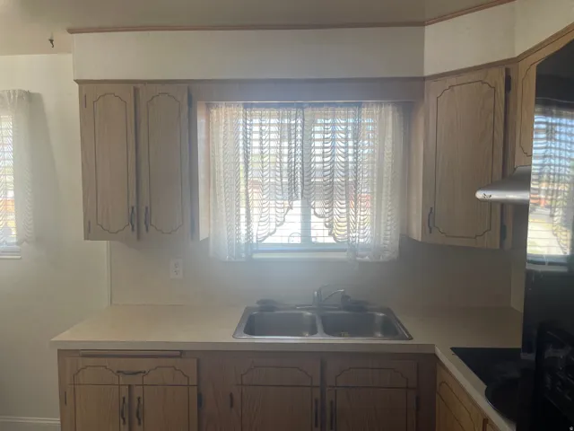 Kitchen featuring light wood-finish cabinetry, a double basin stainless steel sink, and light-toned countertops