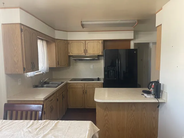 Kitchen featuring wood-finish cabinetry, a black side-by-side refrigerator, a dual basin sink, and a counter-height island