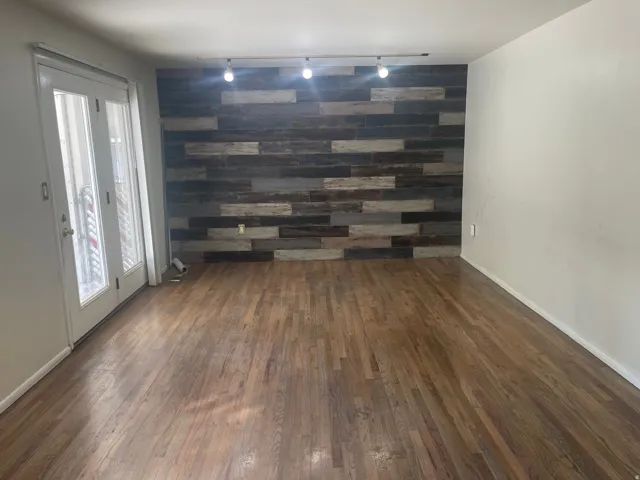 Wood-finish flooring throughout, accent wall featuring varied wood-look paneling, track lighting, and double-paned glass French doors