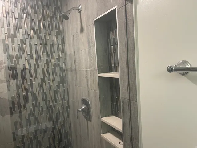 Walk-in shower featuring a decorative tile accent wall, built-in shelving, a rainfall showerhead, and a polished chrome fixture