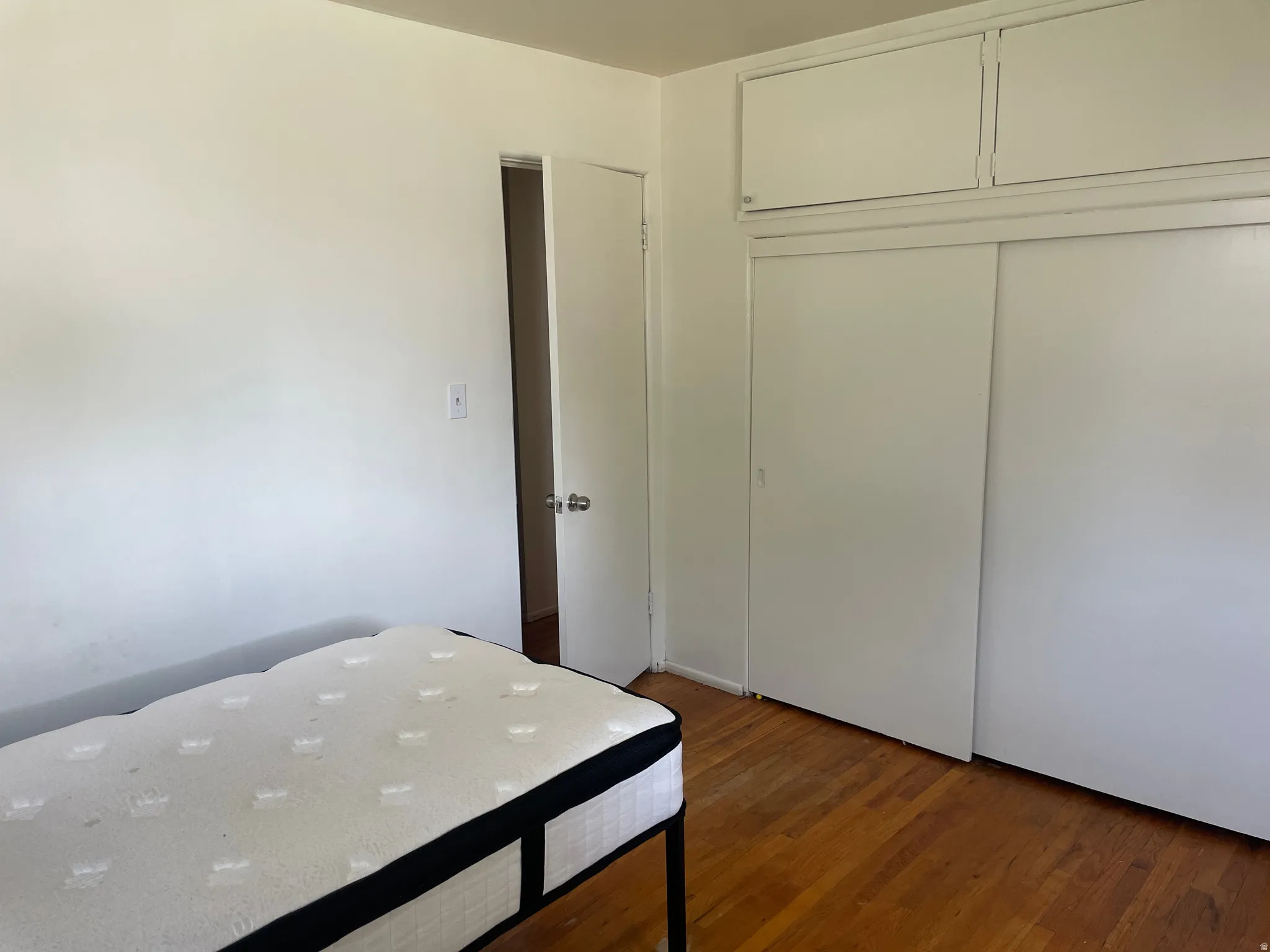 Hardwood flooring throughout featuring white walls and a white interior door