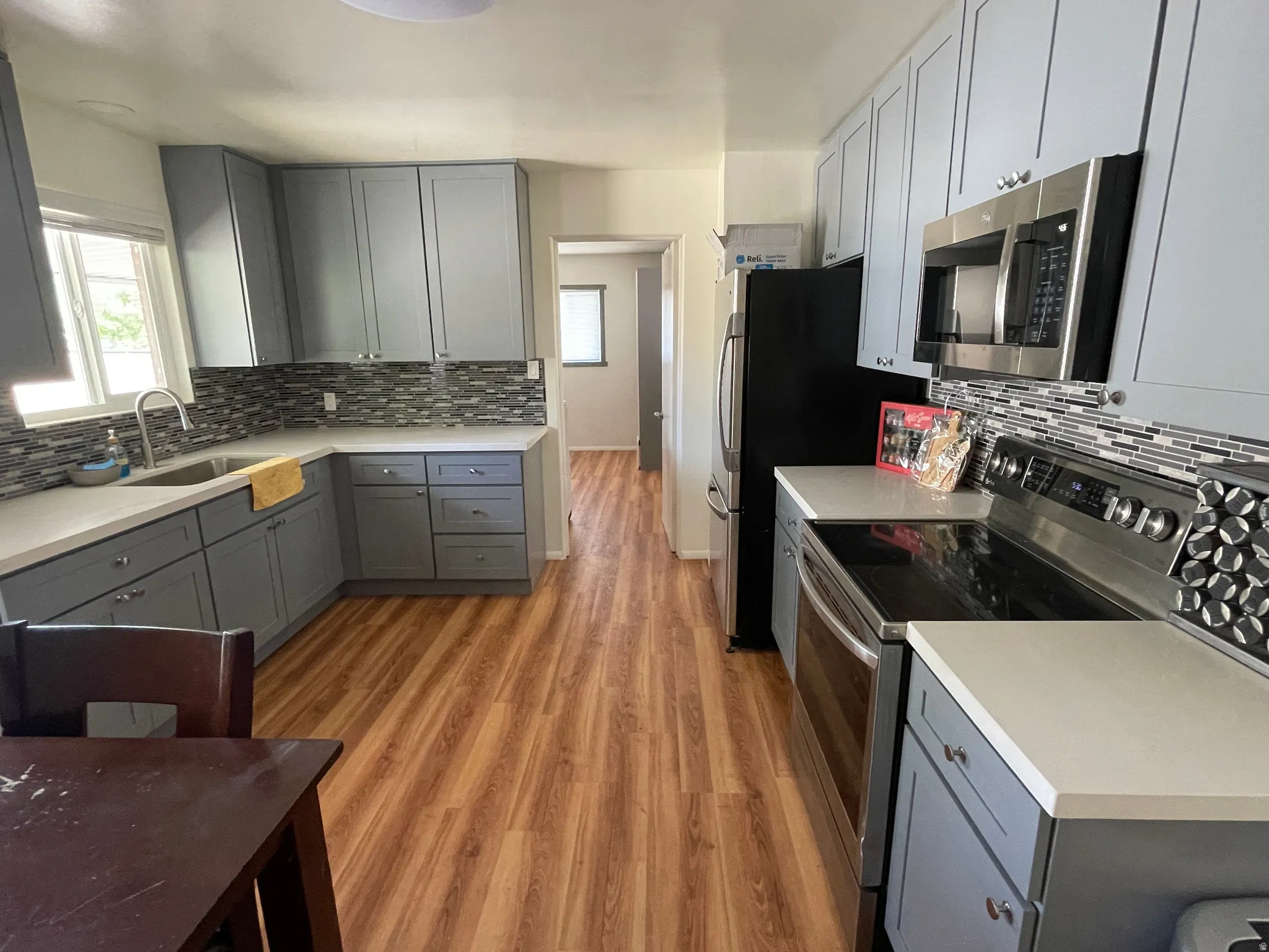 Modern kitchen featuring wood-finish flooring, light grey cabinetry, white countertops, a mosaic tile backsplash, and stainless steel appliances
