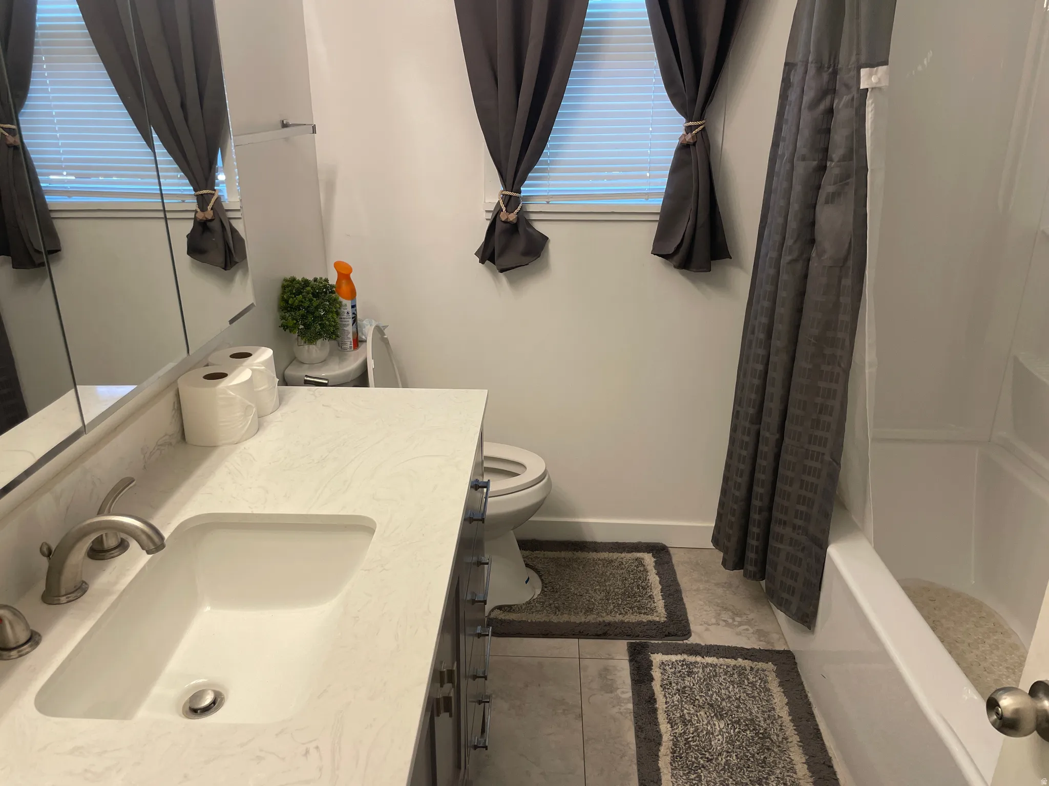 Bathroom featuring a white integrated sink, light-toned countertop, brushed nickel faucet, and a white bathtub with a shower