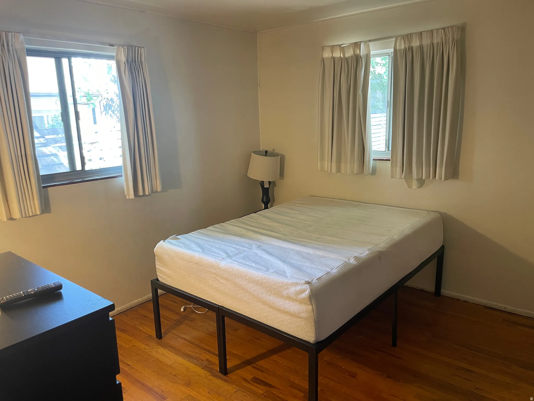 Hardwood flooring throughout featuring two windows with privacy drapery
