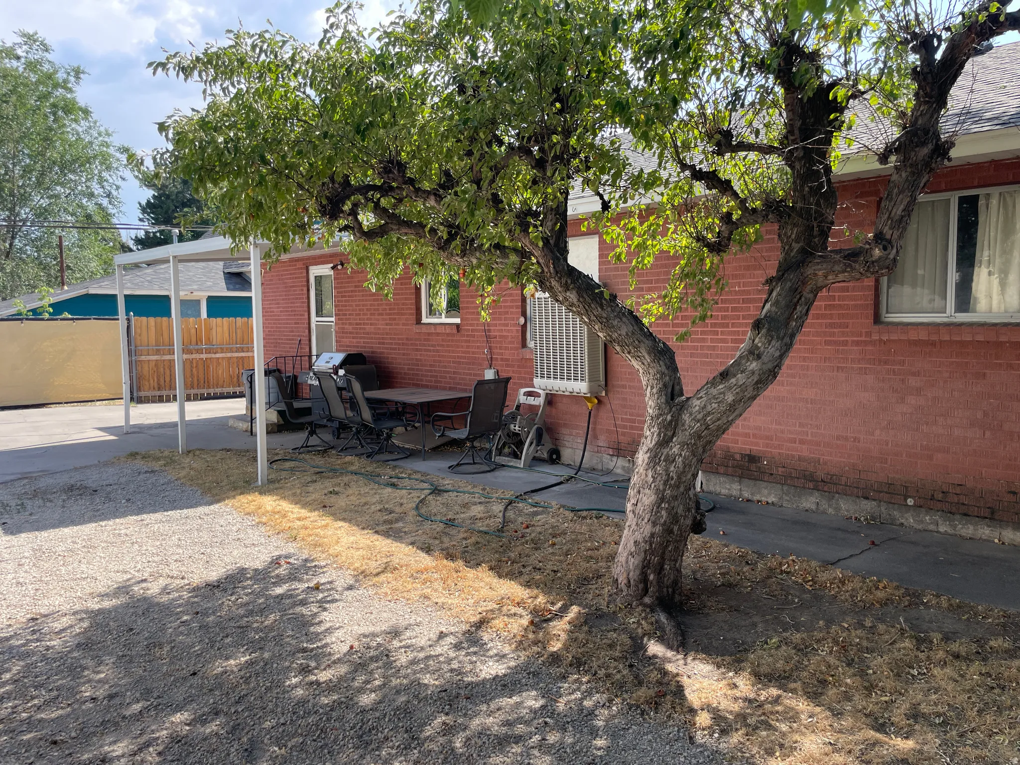Mature tree providing shade to the backyard, red brick exterior, concrete patio, and gravel landscaping