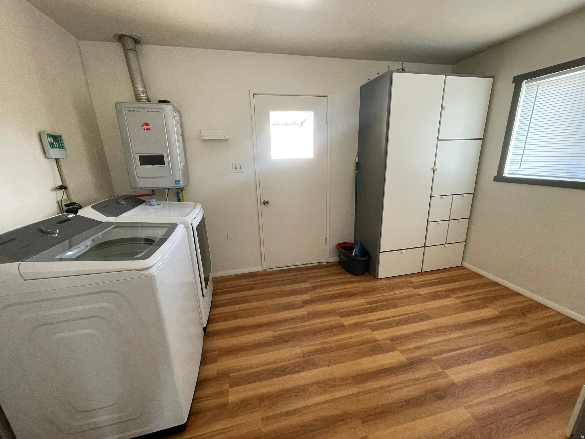 Utility room featuring wood-finish flooring, a contemporary water heater, and built-in storage cabinetry
