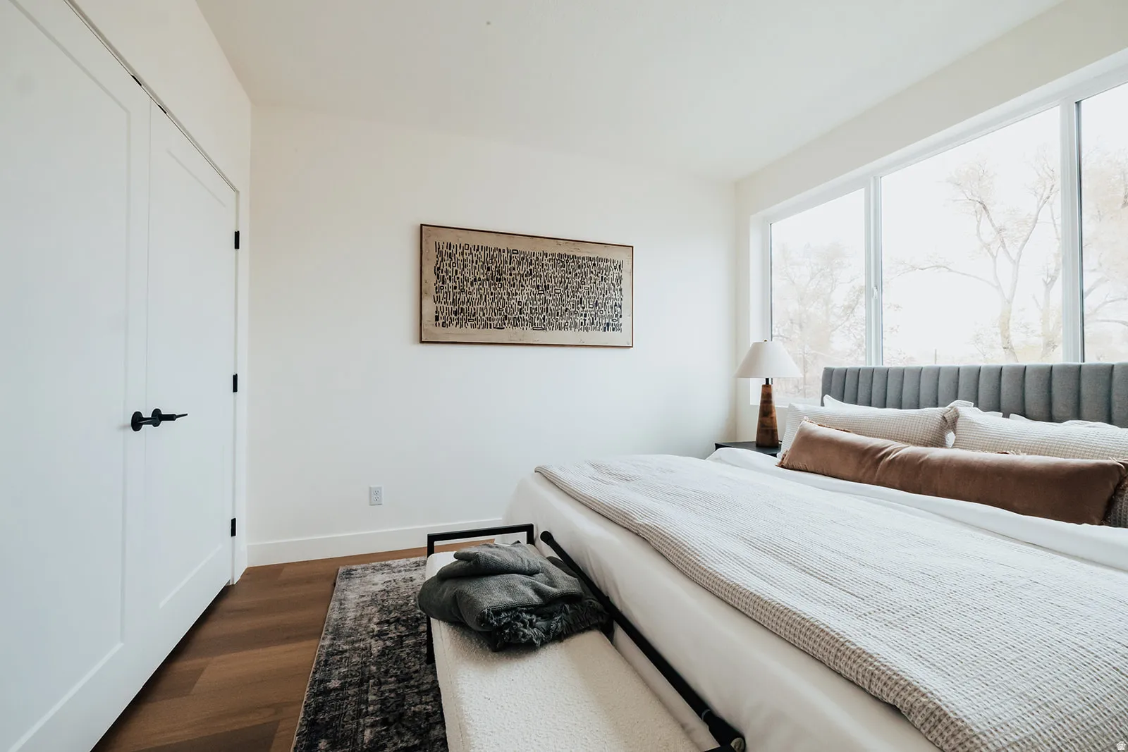 Bright bedroom featuring wide plank wood-finish flooring, white trim, and a full wall of windows