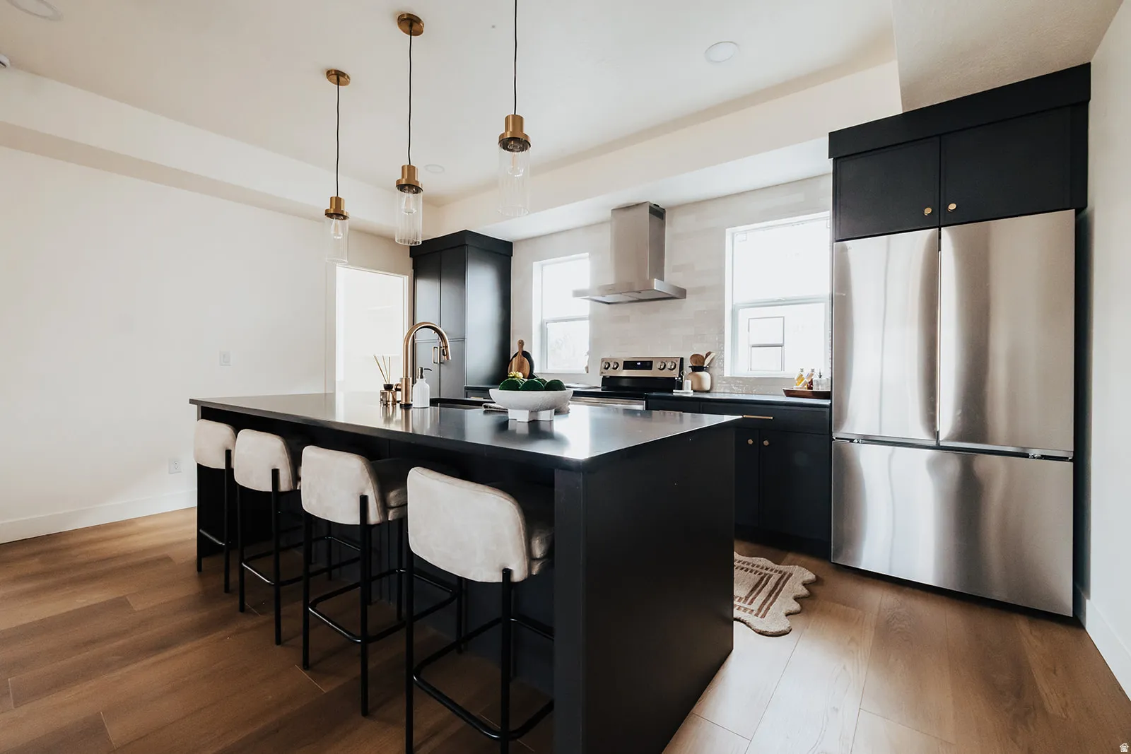 Spacious kitchen featuring an expansive central island with seating, dark cabinetry, stainless steel appliances, and wood-finish flooring