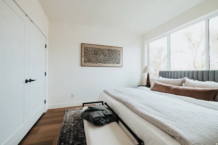 Bright bedroom featuring wide plank wood-finish flooring, white trim, and a full wall of windows