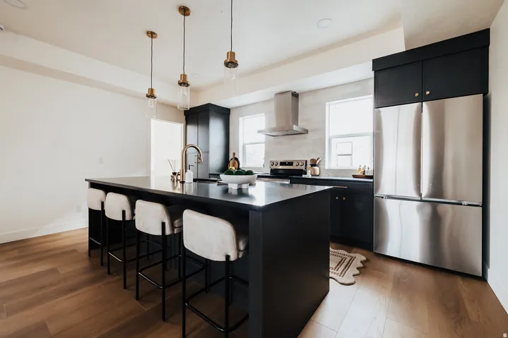 Spacious kitchen featuring an expansive central island with seating, dark cabinetry, stainless steel appliances, and wood-finish flooring