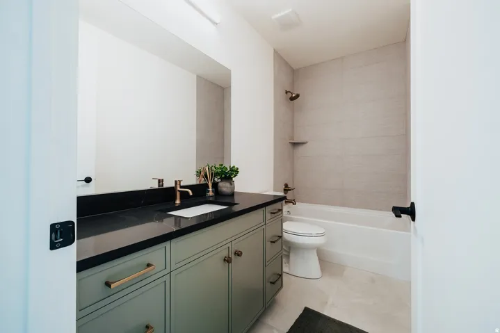 Bathroom featuring a sage green vanity with brass hardware, a dark countertop, an undermount sink, and a large wall mirror