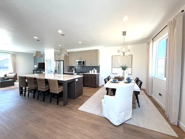 Open-concept living area featuring wood-finish flooring, a kitchen island with seating, pendant lighting, shaker-style cabinetry, and stainless steel appliances
