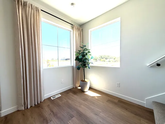 Bright interior space featuring two large windows, wood-finish flooring, light-colored walls, and a contemporary stair handrail