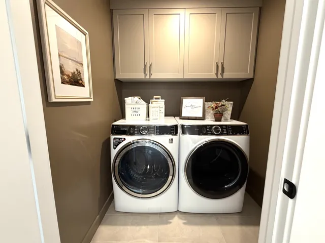 Dedicated laundry area featuring overhead cabinetry, wall-mounted storage, and tile flooring