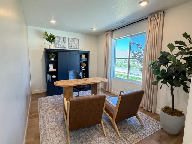 Recessed lighting illuminating wood-finish flooring, a large window with privacy treatments, and a built-in wall unit featuring cabinetry and open shelving