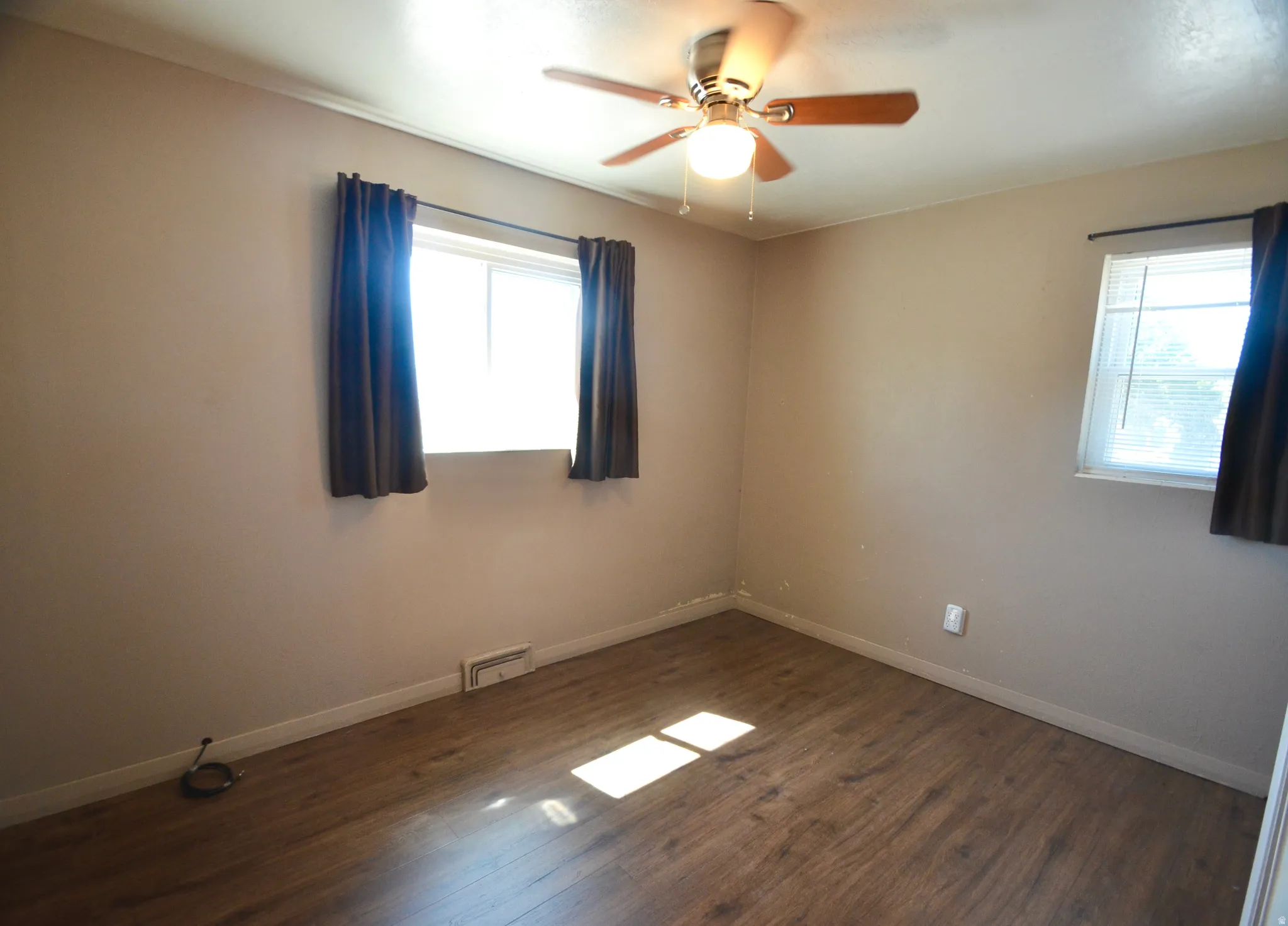 Room with wood-finish flooring, a ceiling fan with integrated lighting, and two windows