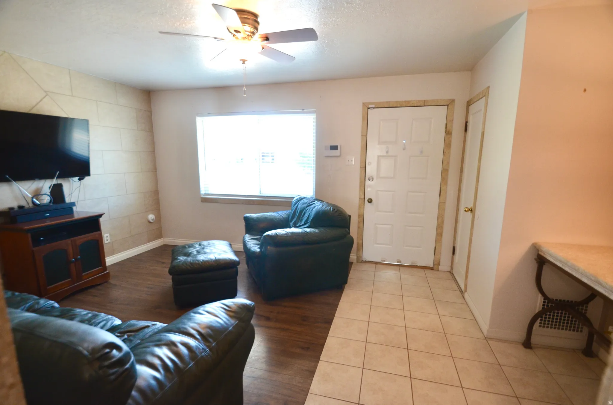 Living area featuring a prominent window, a ceiling fan with light fixture, and wood-finish flooring