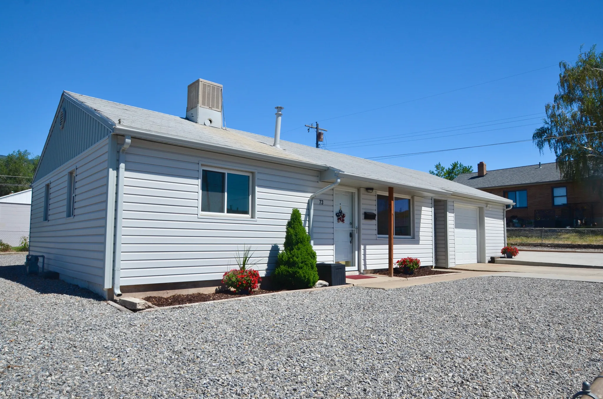 Single-story exterior featuring light-colored siding, a covered front entry, an attached garage, and a gravel driveway
