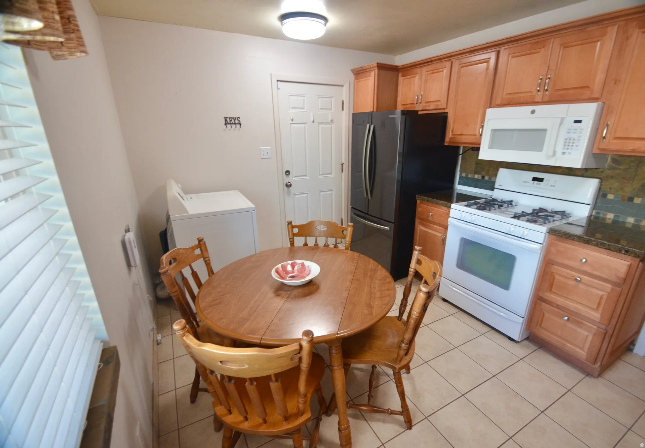 Kitchen featuring light wood cabinetry, dark speckled countertops, a mosaic tile backsplash, and tile flooring