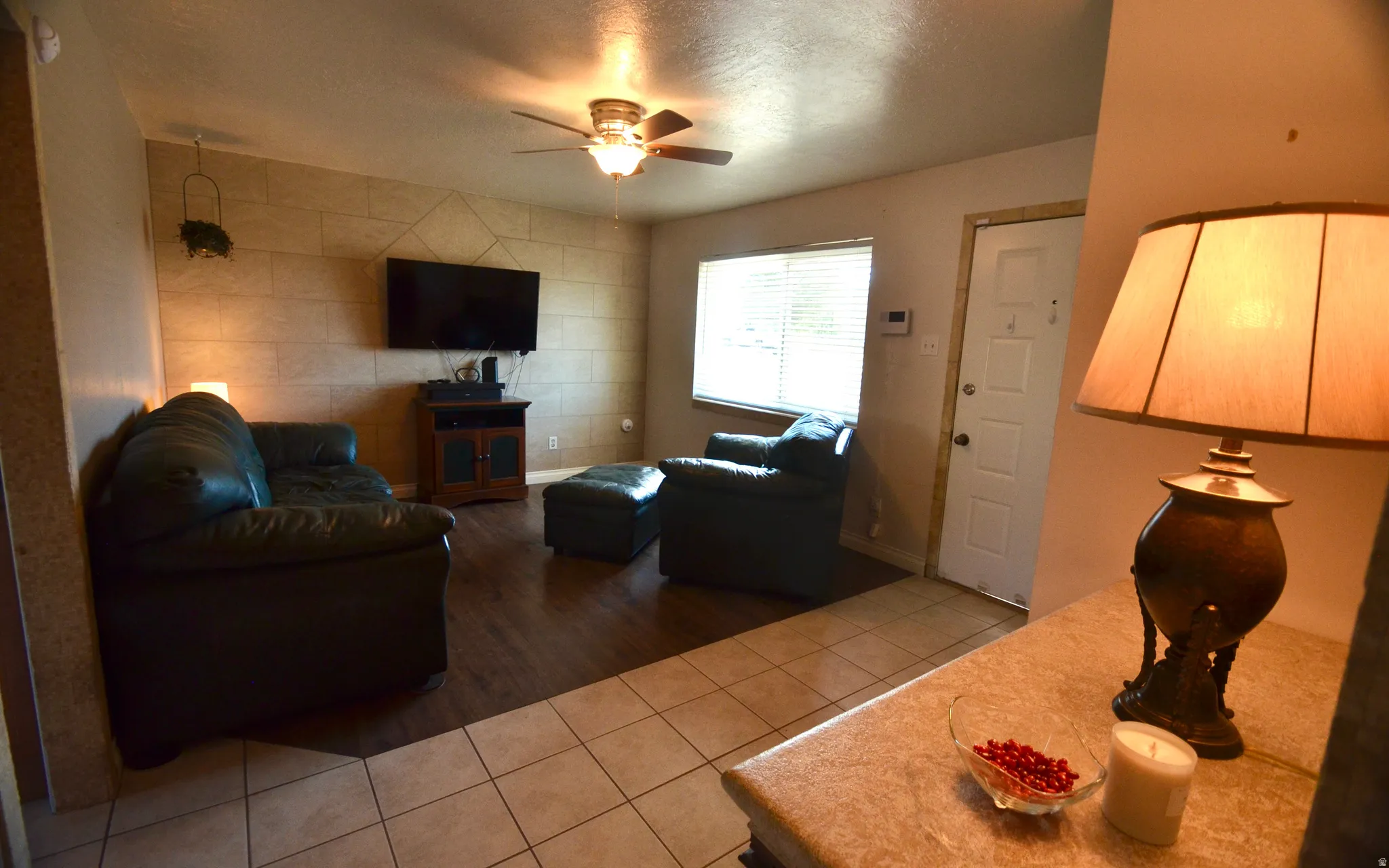 Open living space featuring a textured accent wall, wood-finish flooring, and a ceiling fan with integrated lighting