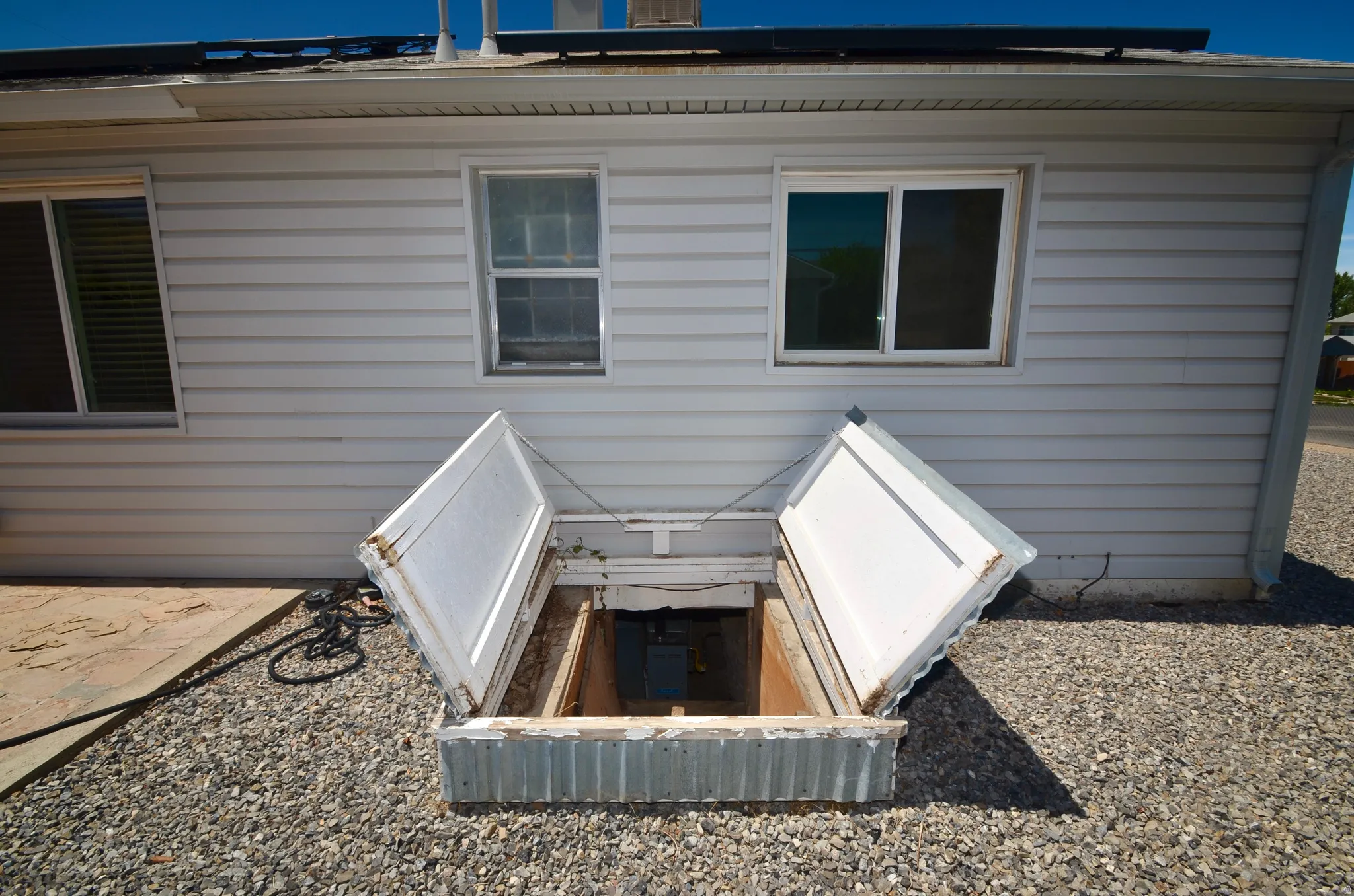 Exterior siding featuring a ground-level basement access with open double doors, gravel landscaping, and dual-pane windows