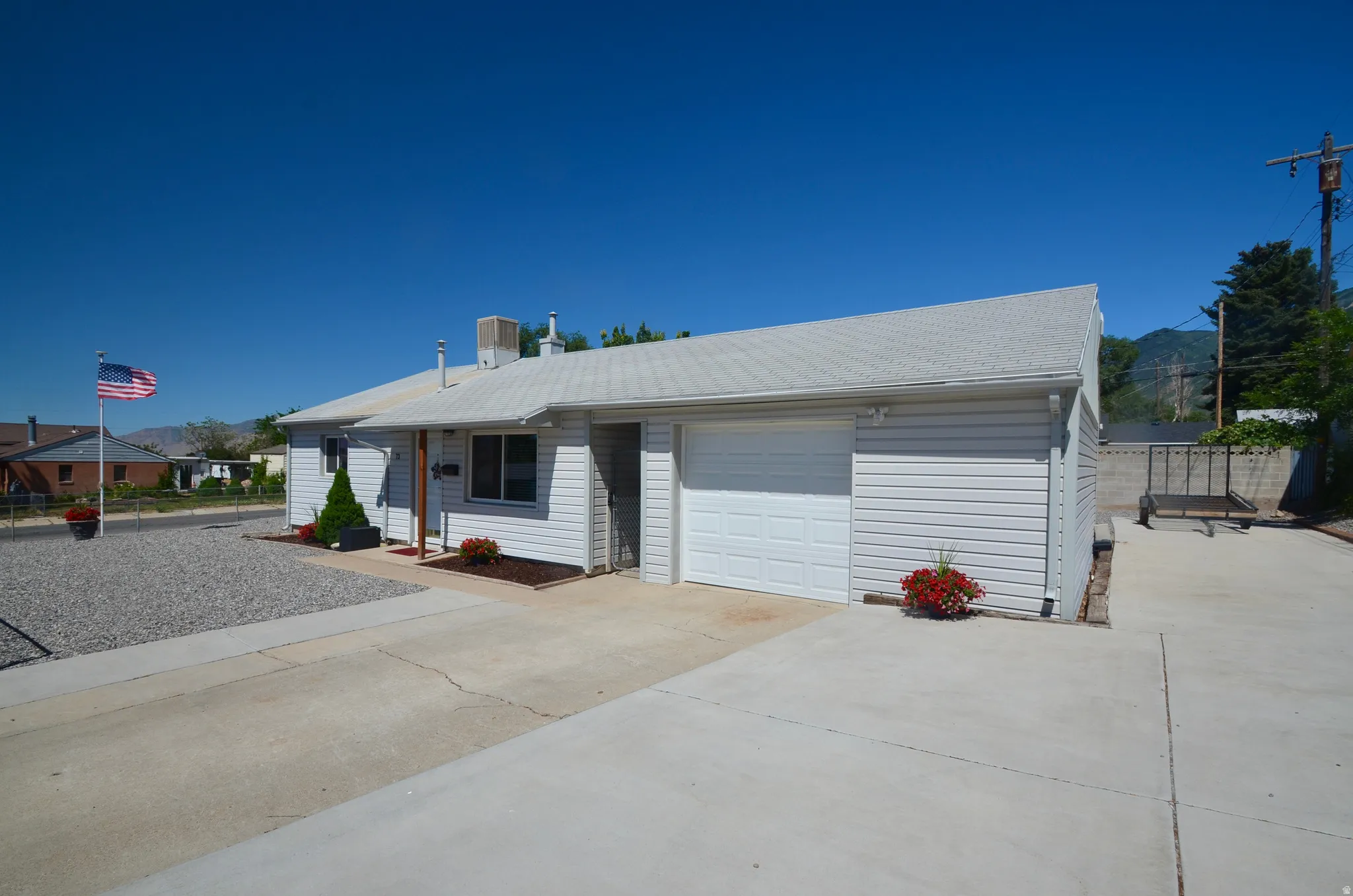 White siding exterior with an attached garage, concrete driveway, and gravel landscaping