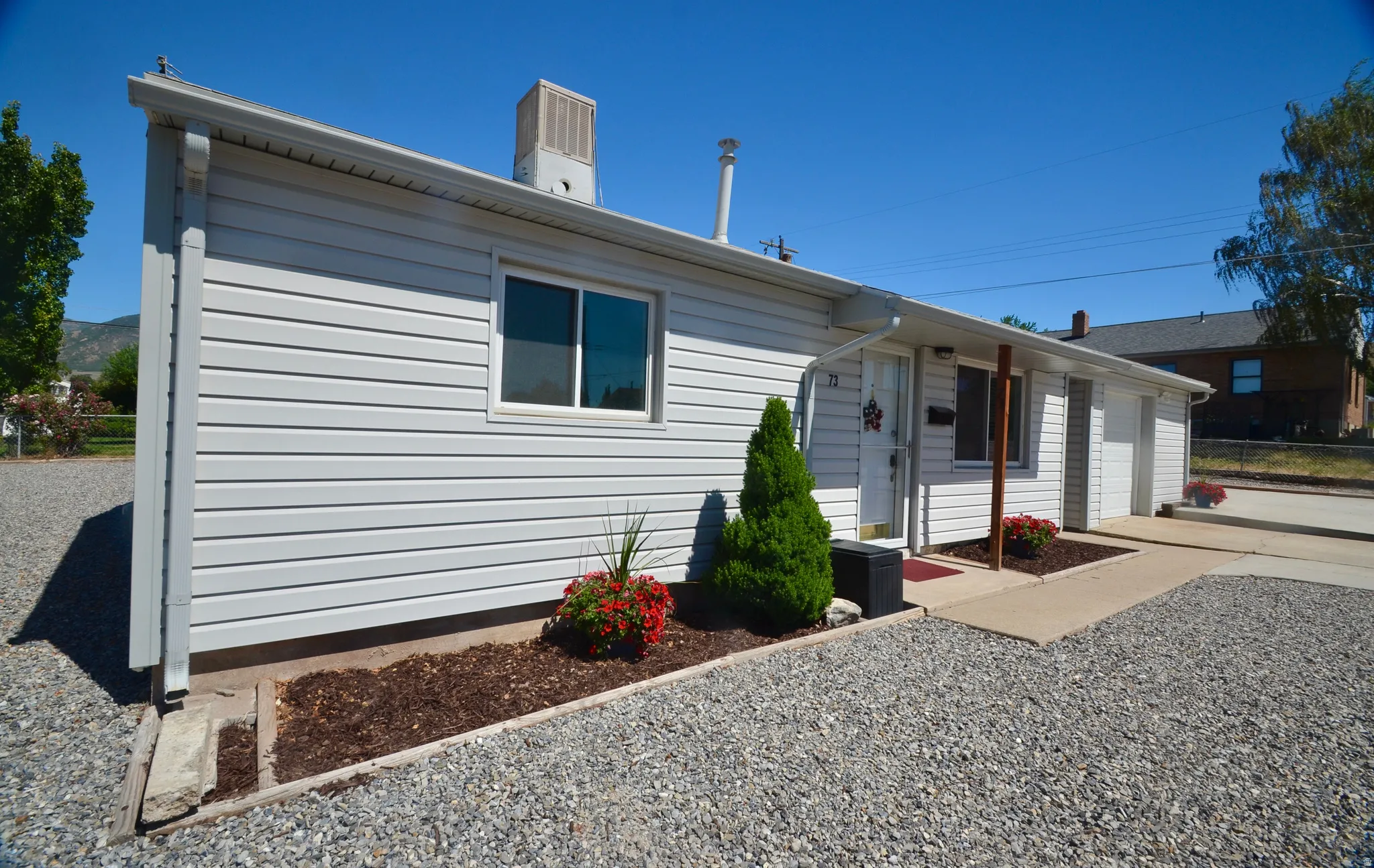 White siding exterior with a covered entryway, a gravel driveway, and landscaped planting beds