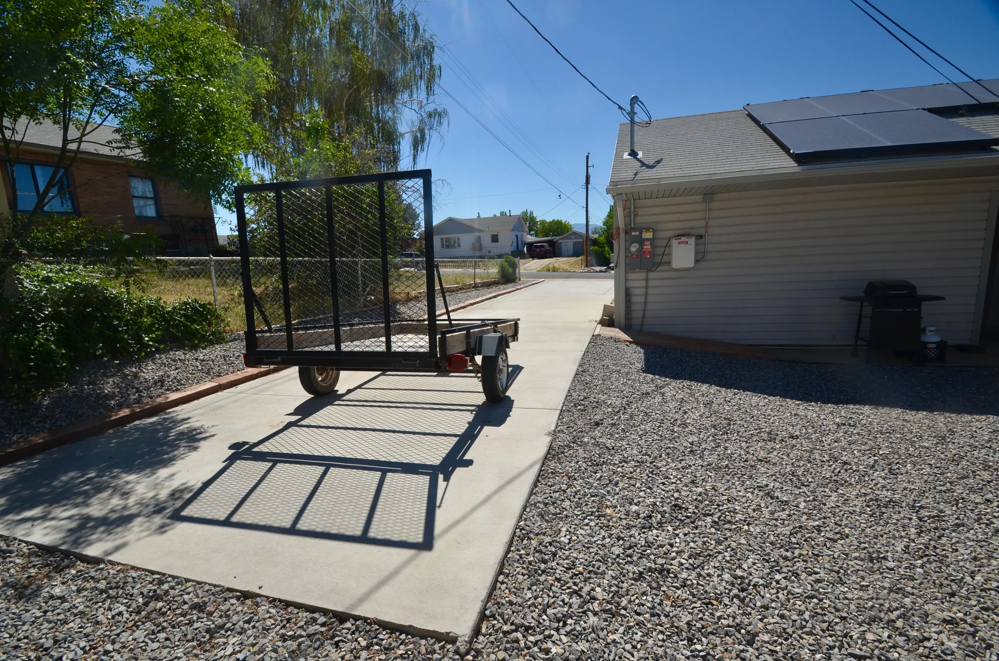 Detached auxiliary building with solar panels, cement driveway, and gravel hardscaping