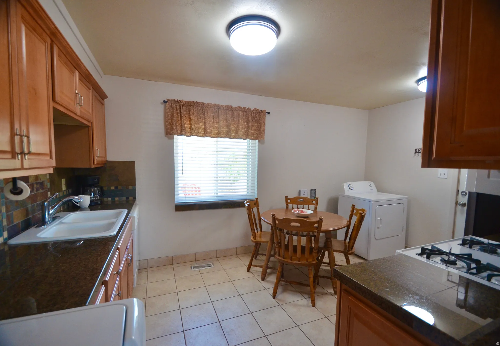 Functional kitchen featuring wood cabinetry, stone-look countertops, and a tiled backsplash