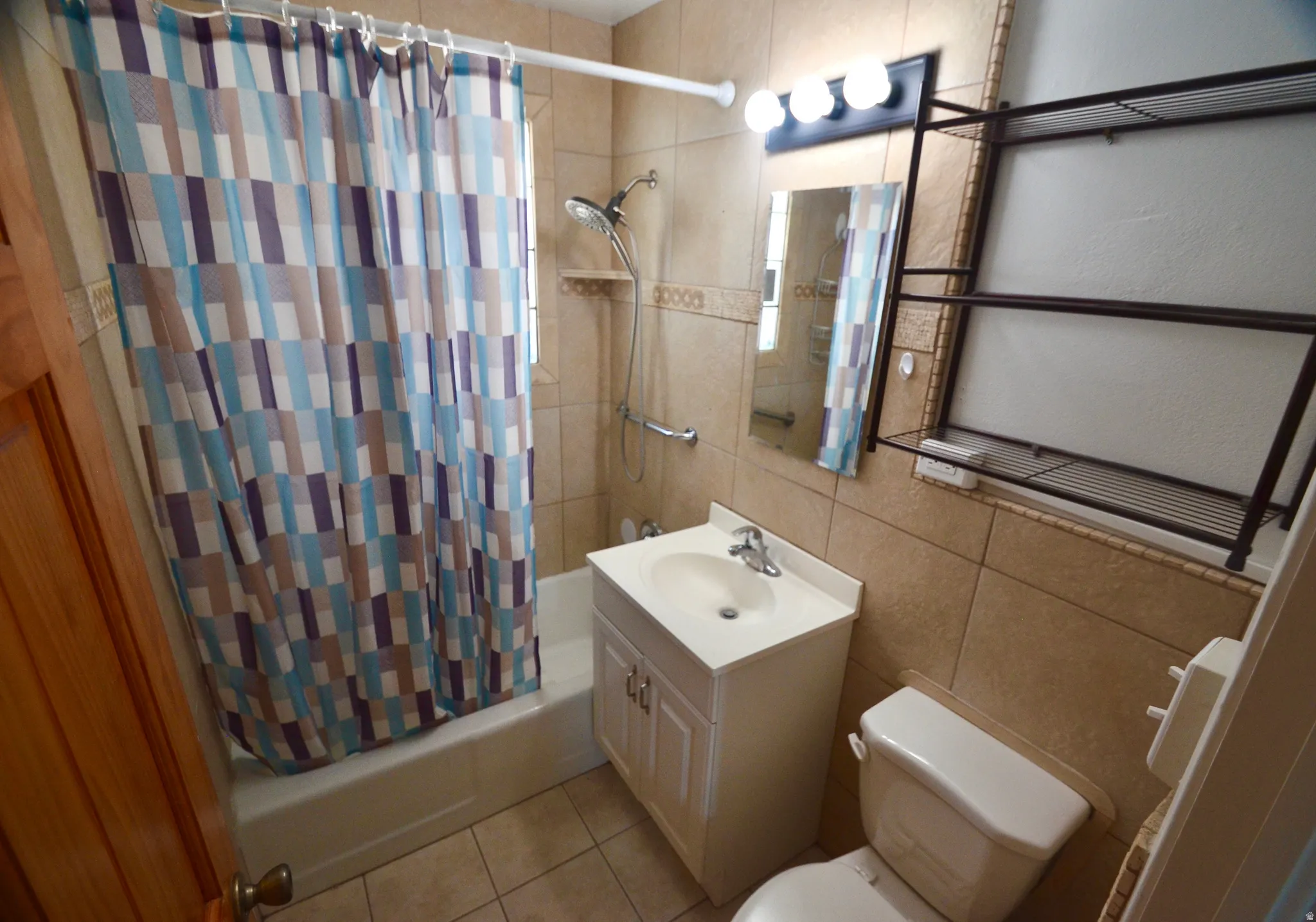 Bathroom featuring neutral-toned floor and wall tiling, a white vanity with integrated sink, a built-in bathtub with shower, and a wall-mounted mirror with vanity lighting