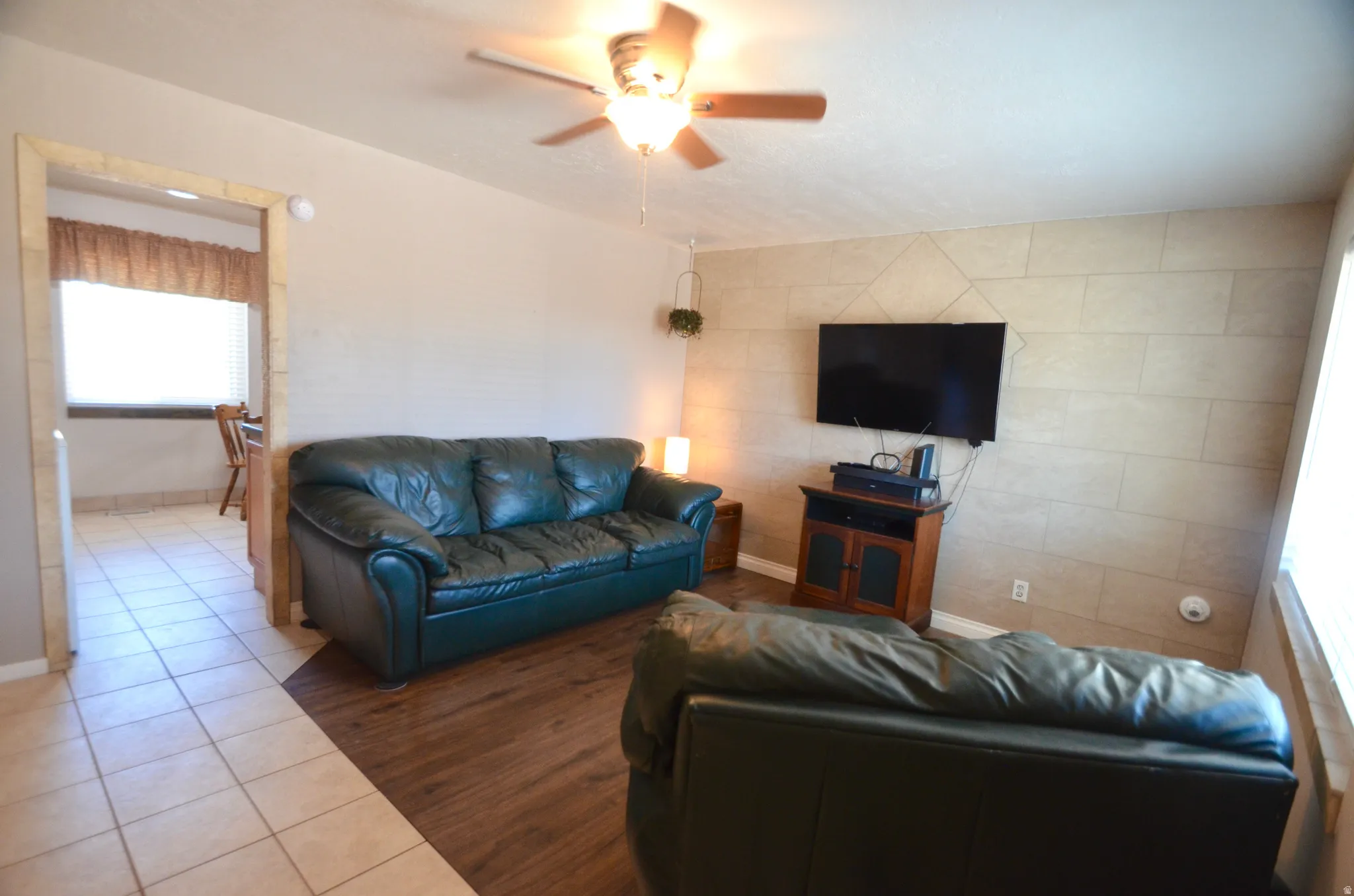 Living area featuring a ceiling fan with integrated lighting, wood-finish flooring, and a decorative accent wall