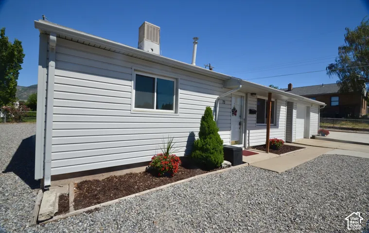 White siding exterior with a covered entryway, a gravel driveway, and landscaped planting beds