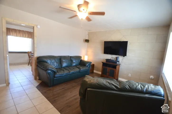 Living area featuring a ceiling fan with integrated lighting, wood-finish flooring, and a decorative accent wall