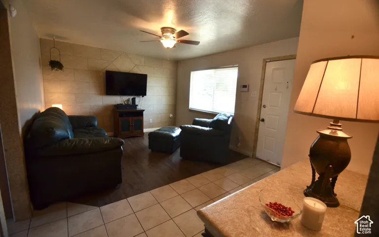 Open living space featuring a textured accent wall, wood-finish flooring, and a ceiling fan with integrated lighting