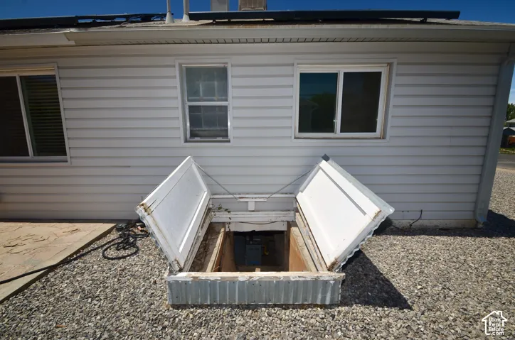 Exterior siding featuring a ground-level basement access with open double doors, gravel landscaping, and dual-pane windows