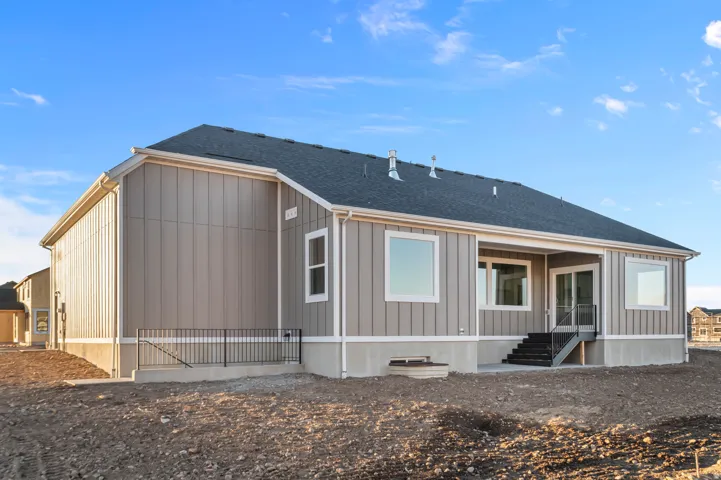 Rear elevation featuring a dark grey shingle roof, tan vertical siding, and a covered patio with sliding glass doors