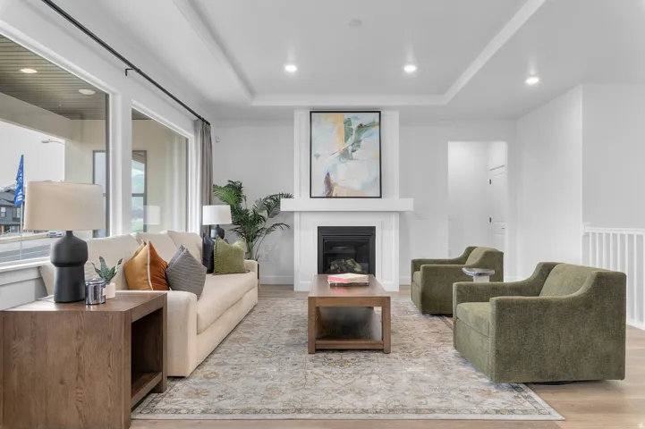 Spacious living area featuring extensive window treatments, a central fireplace with a mantel, recessed ceiling lighting, and wood-finish flooring
