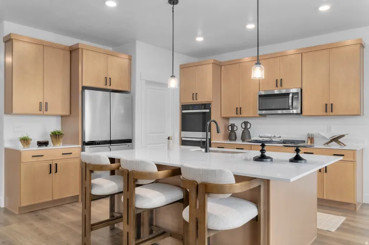 Bright kitchen featuring a central island with countertop seating, light wood-finish cabinetry, stainless steel appliances, pendant lighting, and recessed ceiling lights