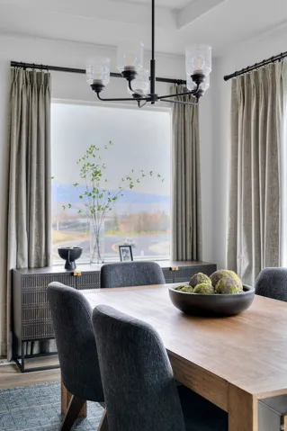 Formal dining area featuring a tray ceiling, a contemporary black chandelier, a large window with neutral drapery, wood-finish flooring, and a textured console table