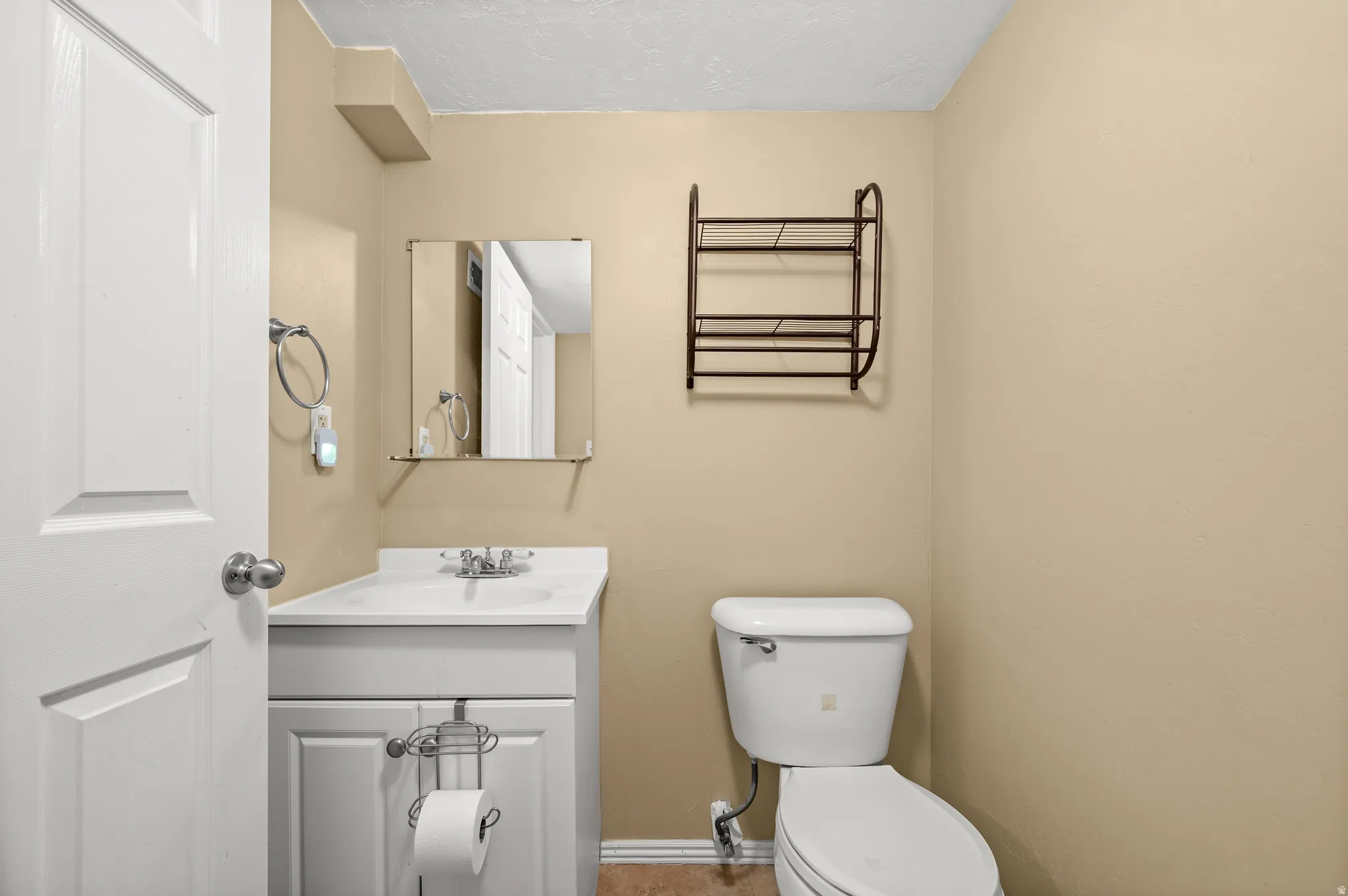 Bathroom featuring a white vanity with integrated sink, chrome faucet, wall-mounted mirror, and a white toilet