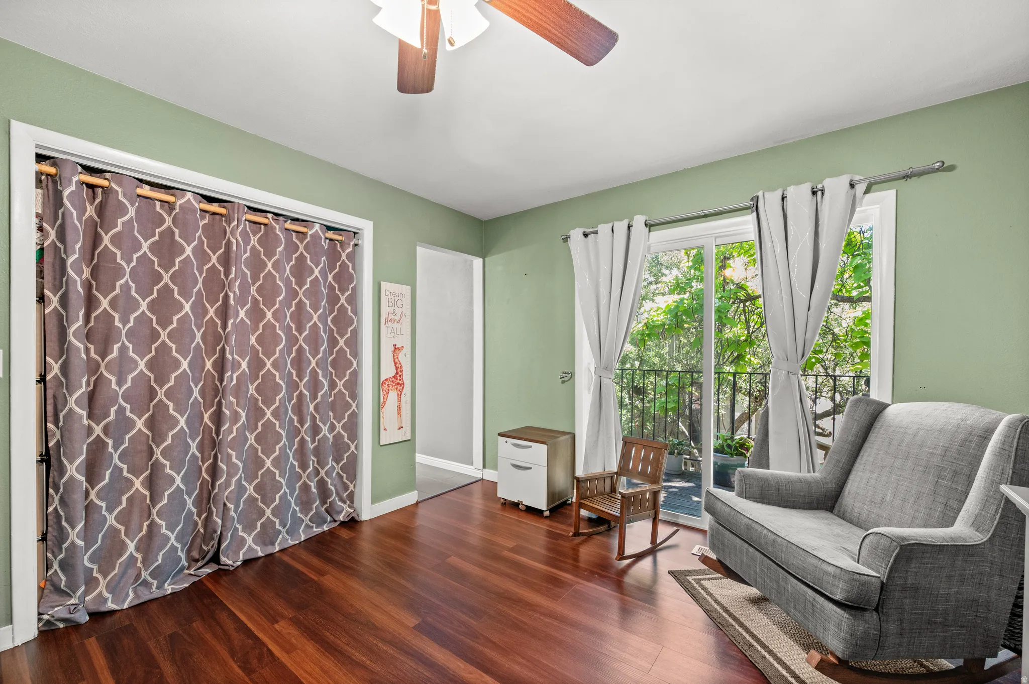 Room featuring wood-finish flooring, light green walls, a ceiling fan, and a sliding glass door leading to an outdoor balcony with a black metal railing
