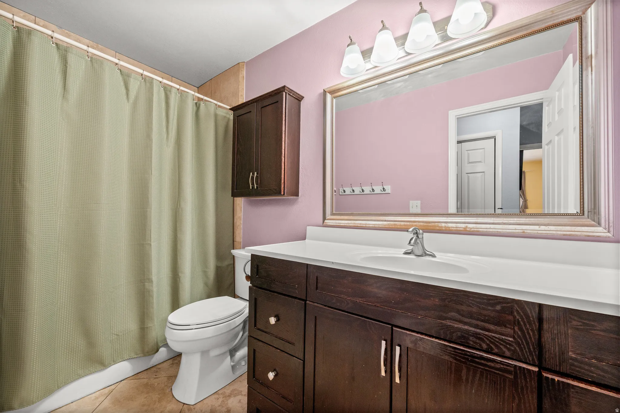 Bathroom featuring a dark wood-finish vanity with a white countertop and integrated sink, a large framed mirror, and a wall-mounted light fixture with four sconces