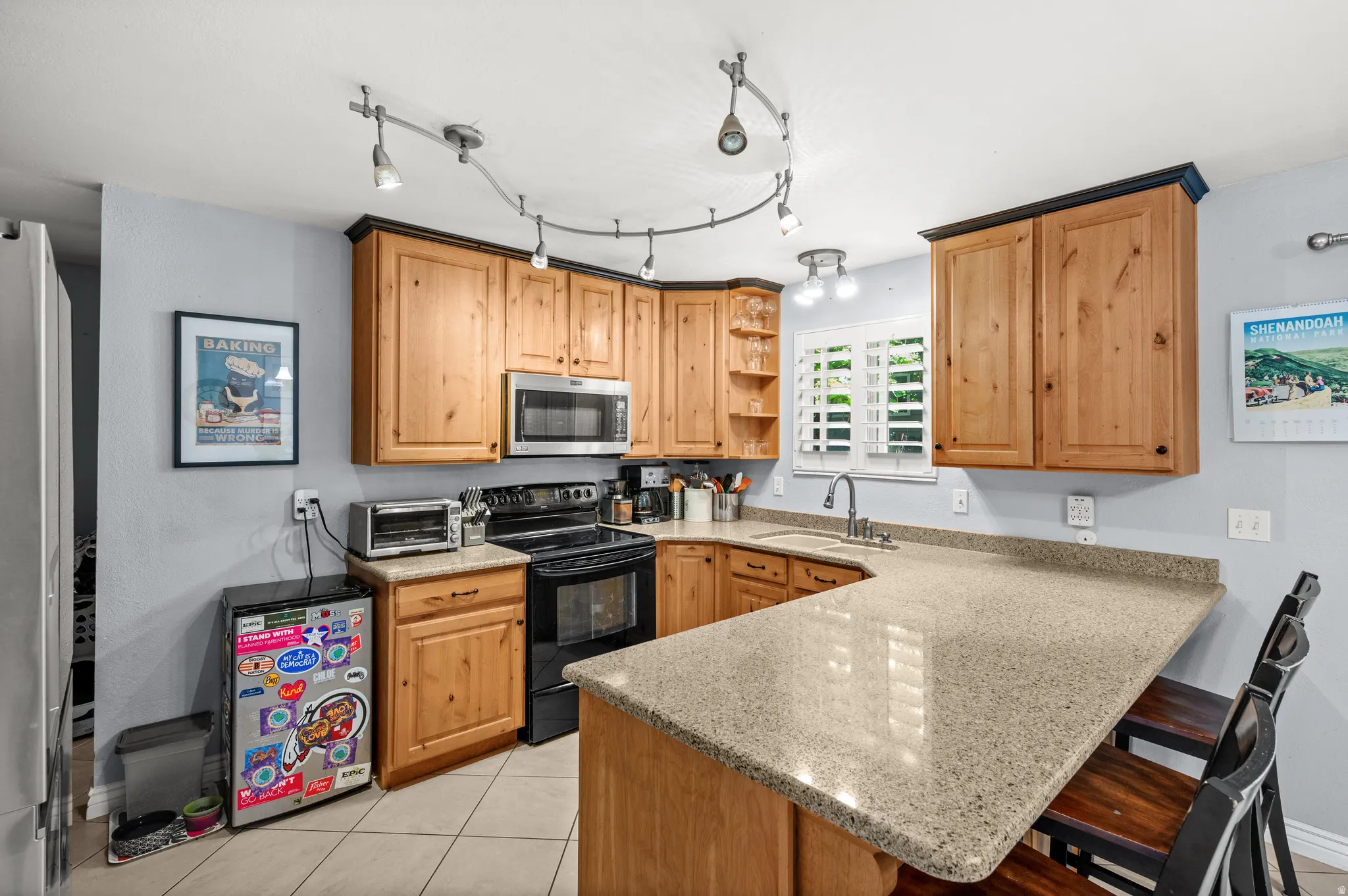 U-shaped kitchen featuring wood cabinetry with dark trim, light-toned countertops, tile flooring, and integrated stainless steel microwave